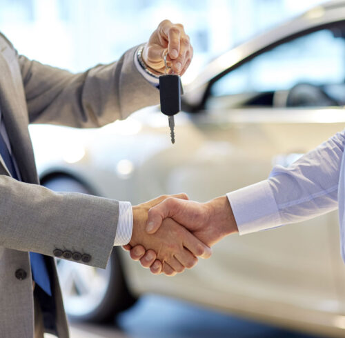 auto business, car sale, deal, gesture and people concept - close up of dealer giving key to new owner and shaking hands in auto show or salon