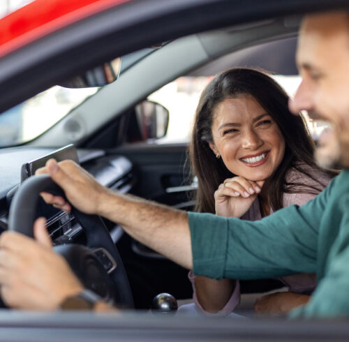 Cute couple sitting in a car at a dealer while deciding whether to buy. Spouses Looking At Car Interior Buying Vehicle In Store. We should organize a test drive